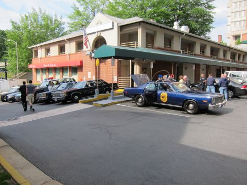 1991 Ford LTD Crown Victoria - Several vintage police cars, including a blue cruiser and black-and-white sedans, are parked outside a motel with a green awning and an Ame…