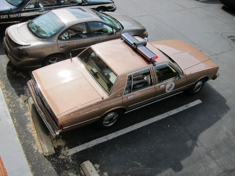 1991 Ford LTD Crown Victoria - overhead view of a tan Chevrolet Caprice police sedan with a roof lightbar and door emblem parked beside a gray sedan.