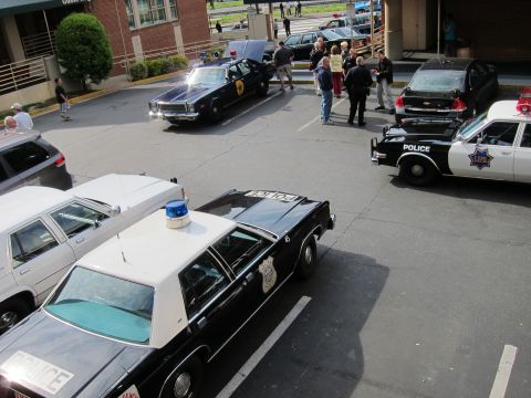 1991 Ford LTD Crown Victoria - elevated view of vintage police cars, including black-and-white and blue cruisers, parked in a lot with people gathered around them.