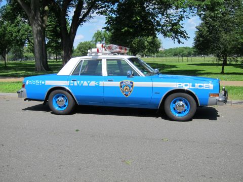 1991 Ford LTD Crown Victoria - Profile of a light blue and white NYPD Highway Patrol sedan marked Police with a roof light bar, parked on a tree-lined roadside.