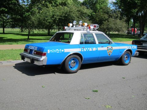 1991 Ford LTD Crown Victoria - Rear view of a light blue and white NYPD Highway Patrol sedan marked Police with roof lights, parked on a tree-lined roadside.