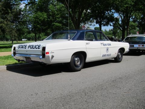 1991 Ford LTD Crown Victoria - Rear view of a white New York State Police sedan with a black roof and single roof beacon, parked on a tree-lined roadside.
