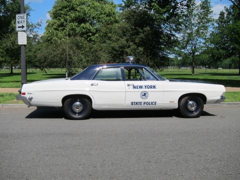 1991 Ford LTD Crown Victoria - Profile of a white New York State Police sedan with black top and tall antenna, parked beside a One Way sign on a grassy roadside.