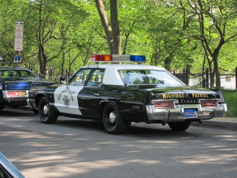 1991 Ford LTD Crown Victoria - Rear view of a black-and-white Highway Patrol sedan with red-and-blue roof lights, parked curbside under green shade trees.