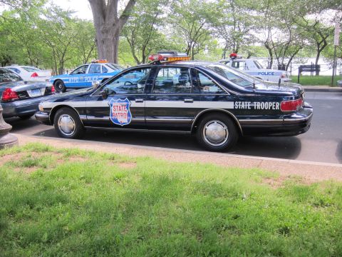 1991 Ford LTD Crown Victoria - black State Trooper Chevrolet Caprice with a red-white-blue State Patrol shield on the door, viewed from the rear three-quarter.