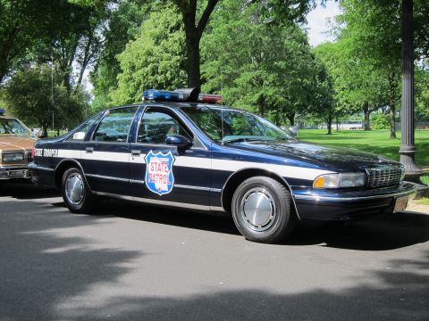 1991 Ford LTD Crown Victoria - dark blue Chevrolet Caprice marked State Trooper with a red-white-blue State Patrol door shield and roof lightbar parked in a park.