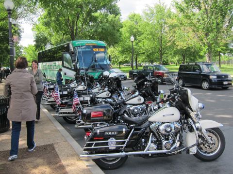 1991 Ford LTD Crown Victoria - row of police motorcycles flying small American flags lined up at a curb in front of a green tour bus and parked cars.
