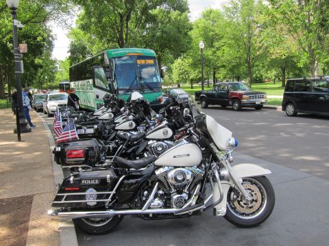 1991 Ford LTD Crown Victoria - Several black-and-white police motorcycles with American flags parked along a curb near a green tour bus and a pickup truck.
