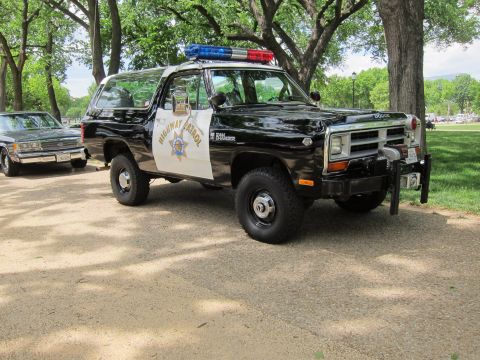 1991 Ford LTD Crown Victoria - Front three-quarter view of a black and white 'Highway Patrol' Dodge Ramcharger SUV with light bar, parked under trees.