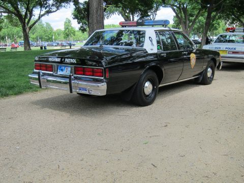 1991 Ford LTD Crown Victoria - Rear three-quarter view of a black and white Chevrolet Caprice 'Highway Patrol' sedan with light bar, parked on a dirt lot.