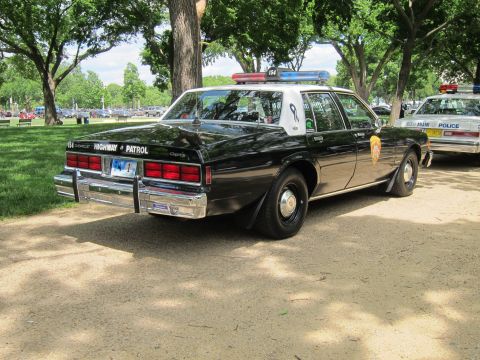 1991 Ford LTD Crown Victoria - black and white Chevrolet Caprice 'Highway Patrol' sedan with a star door shield, parked among other cruisers in a park.