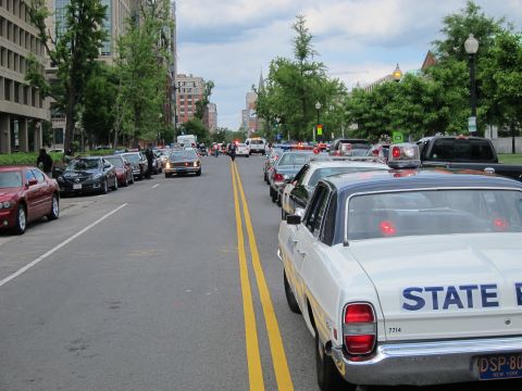 1991 Ford LTD Crown Victoria - white 'State Police' car with New York plate parked along a downtown street amid a line of cruisers and parked cars.