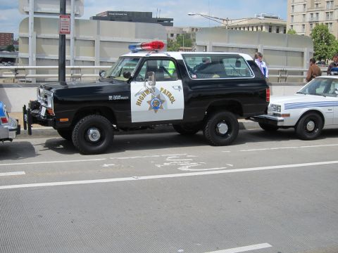 1991 Ford LTD Crown Victoria - black-and-white Dodge Ram Charger SUV marked Highway Patrol parked at a curb between other cars.