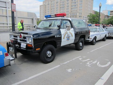 1991 Ford LTD Crown Victoria - black-and-white Dodge Ram Charger SUV in Highway Patrol livery with a roof lightbar parked curbside near other cruisers.