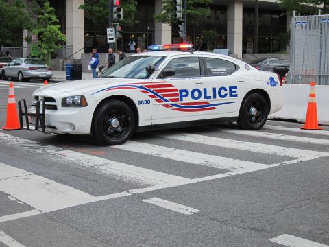 1991 Ford LTD Crown Victoria - white Dodge Charger police car marked POLICE with red and blue striping and a push bar stopped at a crosswalk.