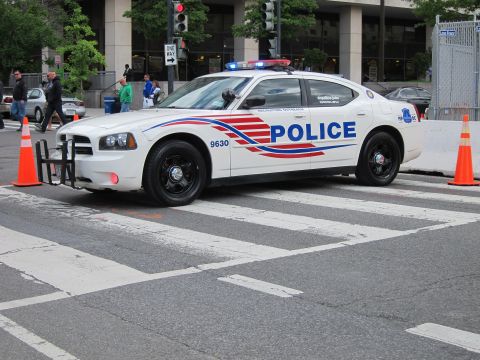 1991 Ford LTD Crown Victoria - white Dodge Charger police cruiser marked POLICE with a push bar and lightbar at a downtown intersection.