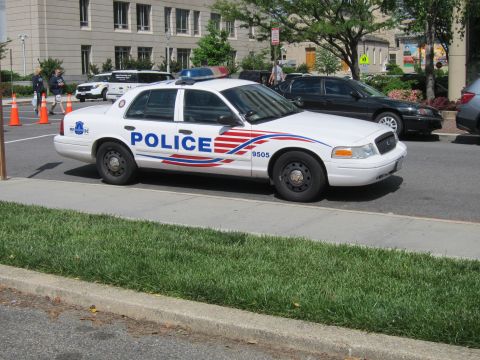 1991 Ford LTD Crown Victoria - white Ford Crown Victoria police cruiser marked POLICE 9505 with red and blue striping parked on a city street.