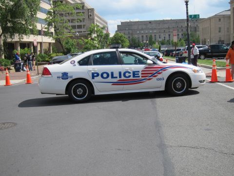1991 Ford LTD Crown Victoria - white Chevrolet Impala police cruiser marked POLICE 1303 with red and blue striping parked on a downtown street.