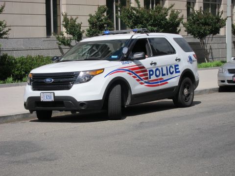 1991 Ford LTD Crown Victoria - white Ford Explorer police SUV marked POLICE with red and blue striping and a lightbar parked at a city curb.