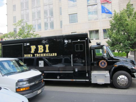 1991 Ford LTD Crown Victoria - black FBI Bomb Technicians box truck with gold lettering parked beside a white van on an urban street.