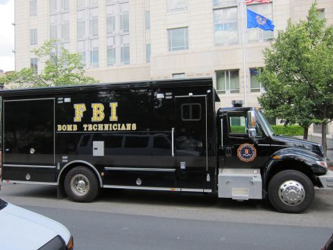 1991 Ford LTD Crown Victoria - side view of a black FBI Bomb Technicians box truck with gold lettering and seal decal parked on a downtown street.