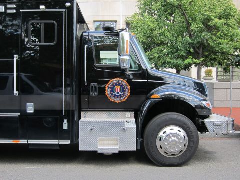 1991 Ford LTD Crown Victoria - close-up of a black FBI truck cab showing the FBI seal decal, chrome side mirror, and front wheel.