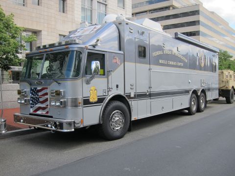 1991 Ford LTD Crown Victoria - large silver Federal Bureau of Investigation Mobile Command Center truck with an American flag graphic parked on an urban street.