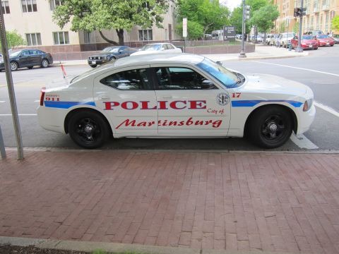 1991 Ford LTD Crown Victoria - Side profile of a white City of Martinsburg police sedan marked 17 with black steel wheels parked at a curb.