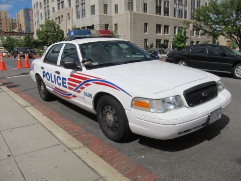 1991 Ford LTD Crown Victoria - white police Ford sedan with red and blue striping and unit 9505 parked along a brick curb in a city.