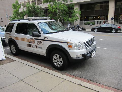 1991 Ford LTD Crown Victoria - white York County Sheriff Ford Explorer SUV with orange striping and unit 29 parked at a city curb.