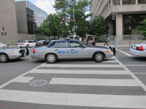 1991 Ford LTD Crown Victoria - silver State Police Ford sedan stopped in a crosswalk at a city intersection between other patrol cars.