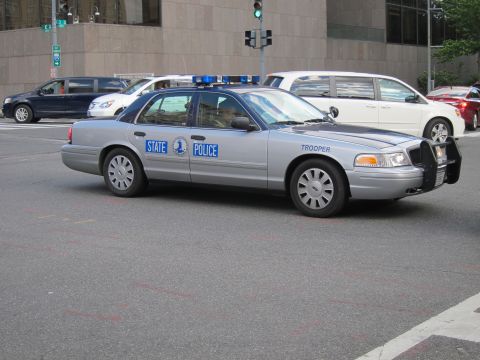 1991 Ford LTD Crown Victoria - silver State Police Ford sedan with activated blue roof lights parked on a downtown street.
