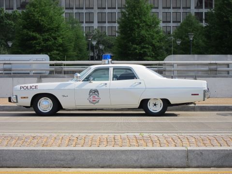 1991 Ford LTD Crown Victoria - white classic Plymouth Fury police sedan marked POLICE, with a single blue dome light, sits curbside in profile.