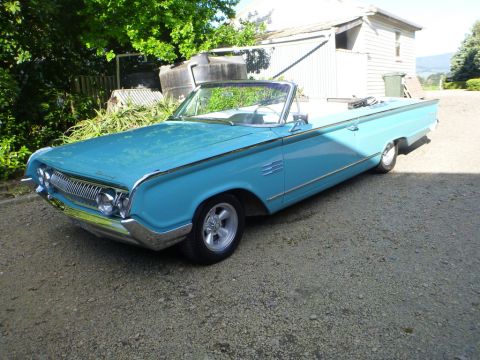 1964 Mercury Monterey - A light blue convertible with chrome accents and a white interior sits parked outdoors on a gravel surface.