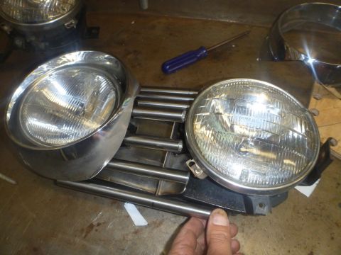 1964 Mercury Monterey - Car headlight assembly with chrome grille and two round headlights is on a workbench.