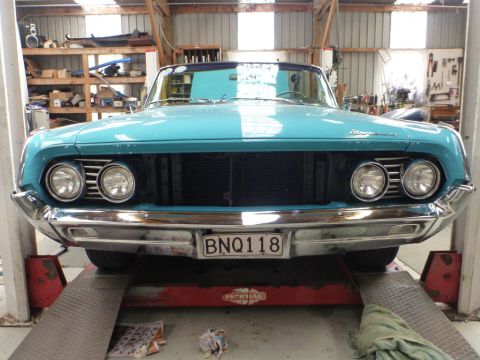 1964 Mercury Monterey - A turquoise convertible is positioned on a lift inside a garage, showing its front grille and headlights.