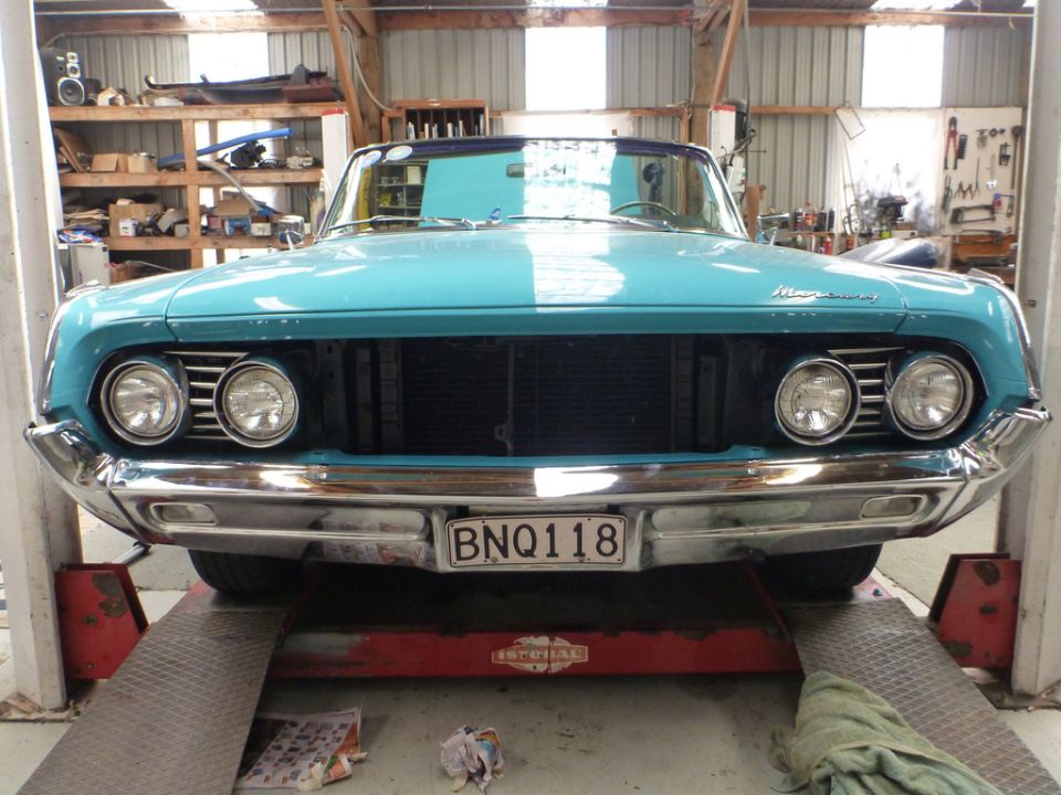 Blue convertible on a lift, front view. Dual headlights, chrome bumper, license plate BNQ118