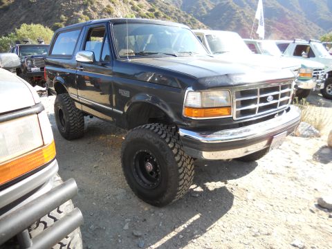1986 Ford Bronco - A dark blue Ford Bronco with lifted suspension and off-road tires is parked in an outdoor setting with other vehicles.