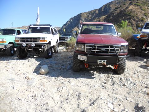 1986 Ford Bronco - Several lifted Ford Broncos are parked off-road in a rocky, mountainous area.