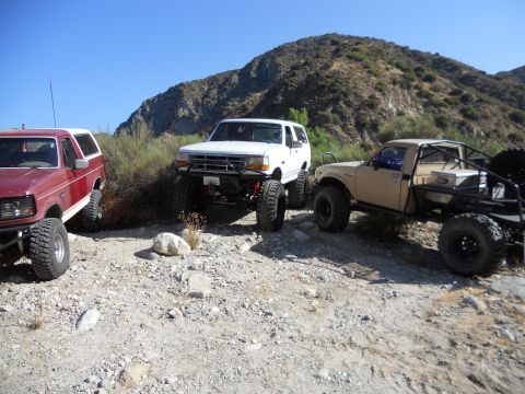 1986 Ford Bronco - A red Ford Bronco, a white Ford Explorer, and a tan Toyota pickup truck are parked on a rocky hillside.
