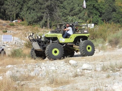 1986 Ford Bronco - A heavily modified jeep navigates a rocky trail in a wooded area.
