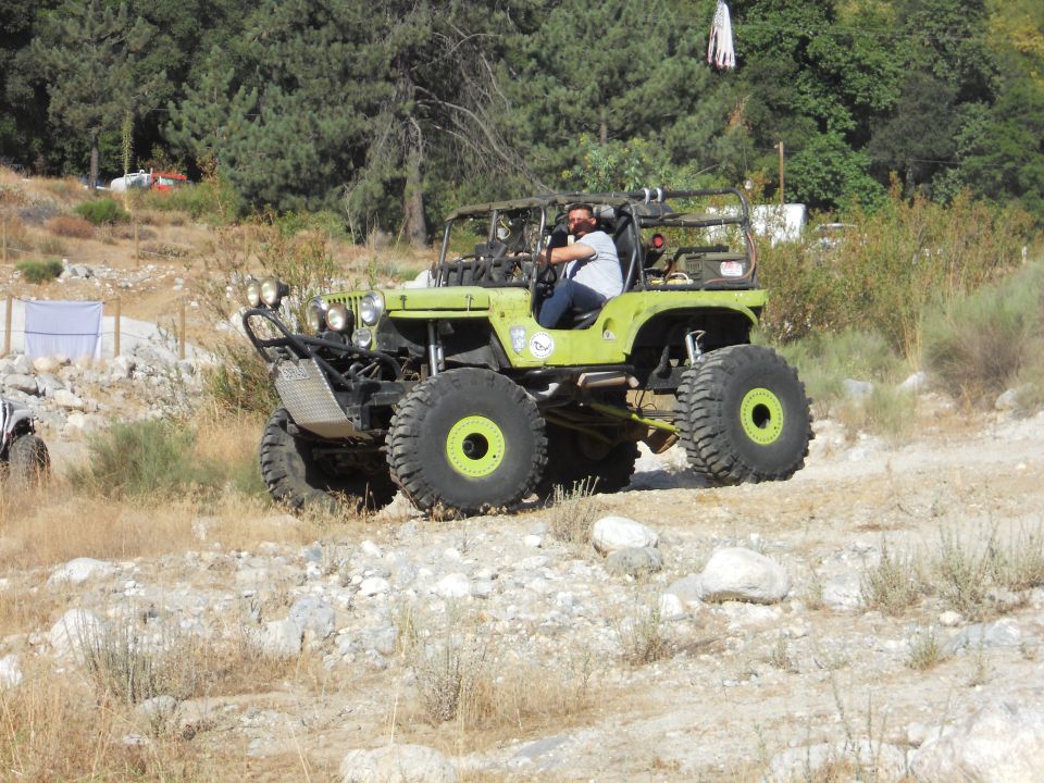 Modified green jeep with large tires and roll cage driving on a dirt path