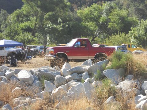 1986 Ford Bronco - A red Ford Bronco with off-road modifications is parked in a rocky, outdoor area with other vehicles present.