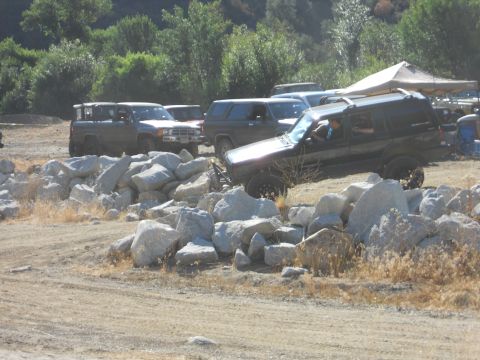 1986 Ford Bronco - Several SUVs and trucks are seen navigating a rocky off-road course under a sunny sky.