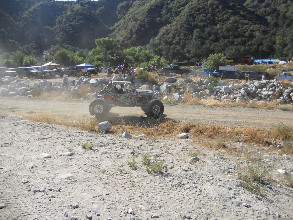 Off-road buggy kicking up dust on a dirt track with other vehicles in background