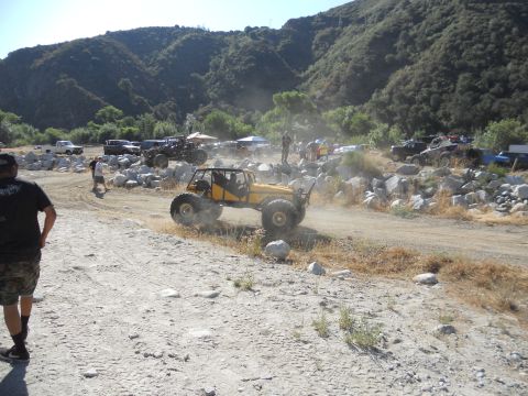 1986 Ford Bronco - Several off-road vehicles are gathered in a rocky, dusty area with mountains in the background.