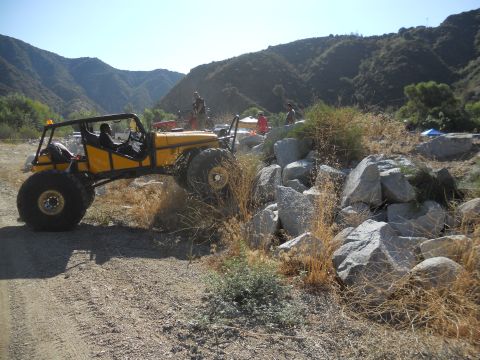 1986 Ford Bronco - A custom yellow off-road buggy navigates a rocky terrain on a sunny day.