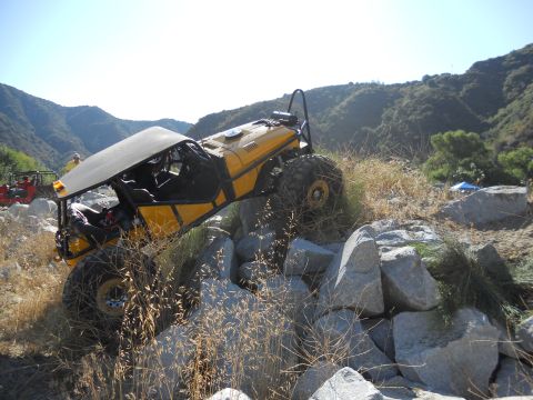 1986 Ford Bronco - A modified off-road vehicle tackles a challenging rocky path in a mountainous area.