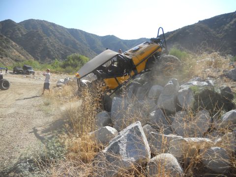 1986 Ford Bronco - A yellow off-road vehicle navigates a rocky terrain with spectators nearby.