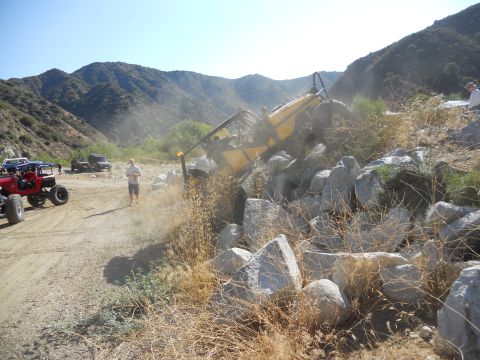 1986 Ford Bronco - An off-road vehicle is stuck on a rocky incline, with spectators observing the scene.